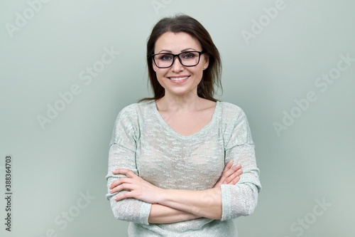 Middle aged smiling happy woman in glasses with crossed arms over green background