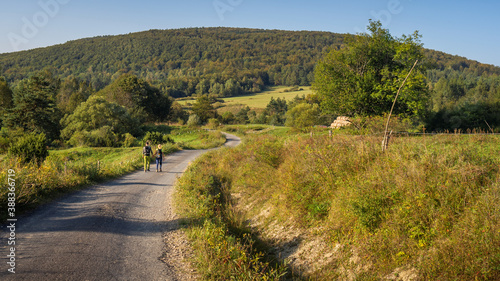 Two people walking together on dirt road in beautiful landscape Beskid Niski mountains view. Couple holding hands while hiking. Regietow Wyzny, Poland, Europe. photo