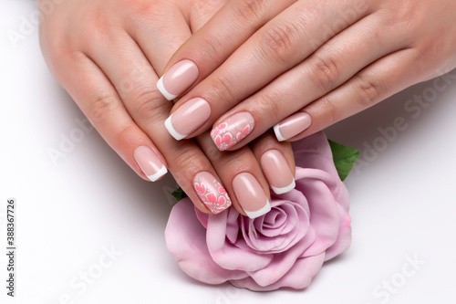 Classic French manicure on short square nails with flowers on the ring fingers. Wedding nail designs. Pink rose in hands.