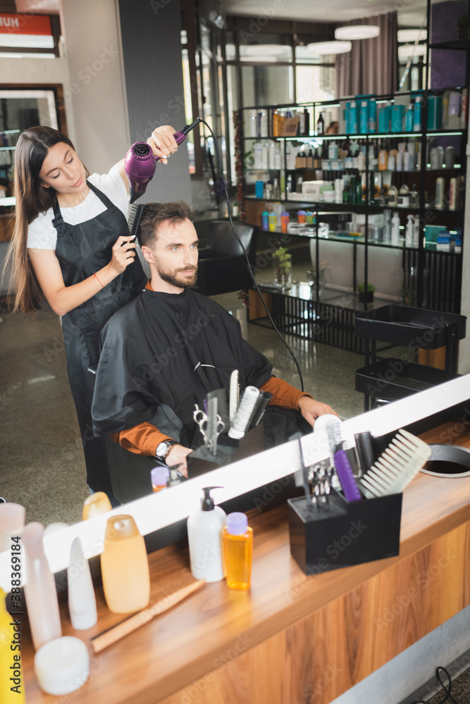 mirror reflection of hairdresser drying hair of client with cosmetic bottles on blurred foreground mirror reflection of hairdresser drying hair of client with cosmetic bottles on blurred foreground
