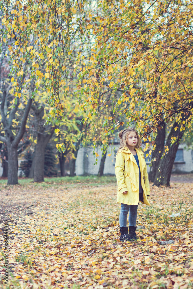 Little beautiful girl in a yellow raincoat walks in the park. Little beautiful girl in a yellow raincoat walks in the park.
