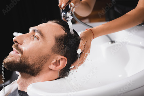 hairdresser washing hair of young, bearded client in barbershop