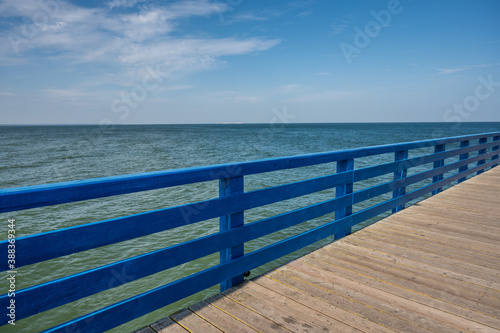 Fototapeta Naklejka Na Ścianę i Meble -  Pier from boards with blue fence against the sea and blue sky with clouds on a sunny day, copy space