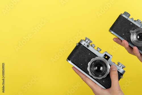 two hands holding two vintage photo cameras on a yellow background with a space for a text.