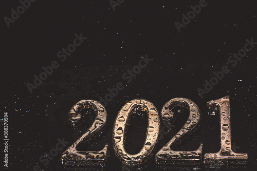 Metallic numbers 2021 in golden color covered with water droplets on a dark background