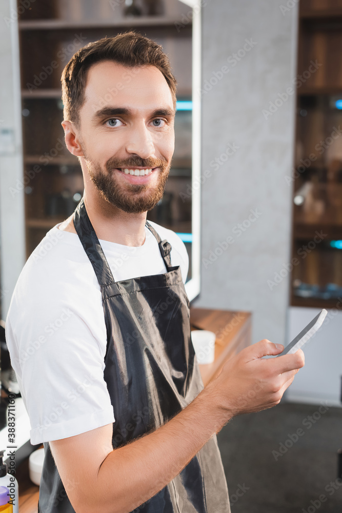 cheerful, bearded hairstylist looking at camera while chatting on smartphone cheerful, bearded hairstylist looking at camera while chatting on smartphone