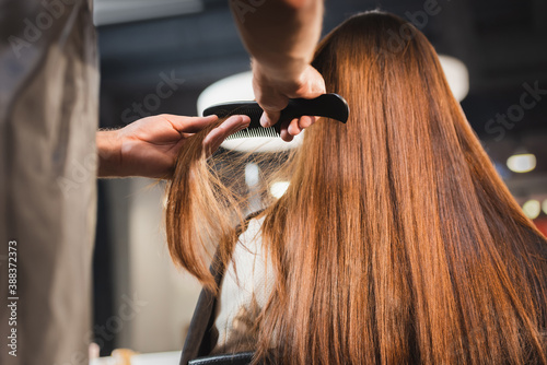 hairdresser combing hair of woman on blurred foreground