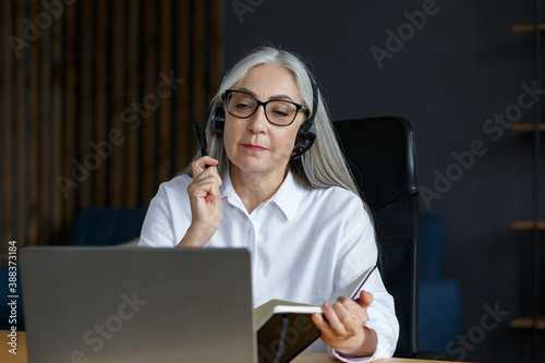 Portrait of beautiful smiling elderly woman studying online. Online education, remote working, home education. Grey-haired senior woman writing in notebook. Mature people study courses online.