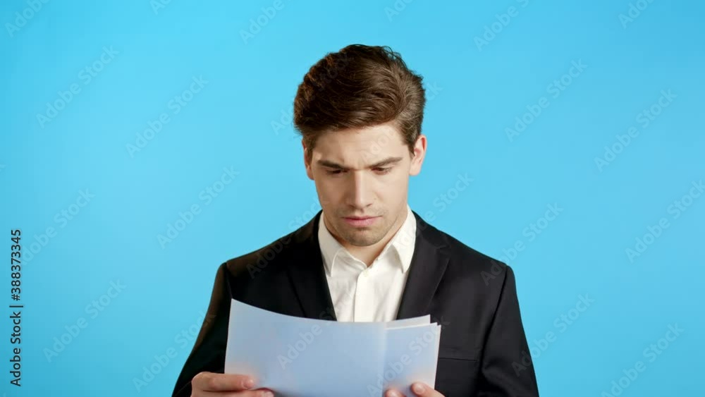 Serious businessman boss isolated on blue background studio. Young male office employee in suit jacket checking documents, reports Serious businessman boss isolated on blue background studio. Young male office employee in suit jacket checking documents, reports