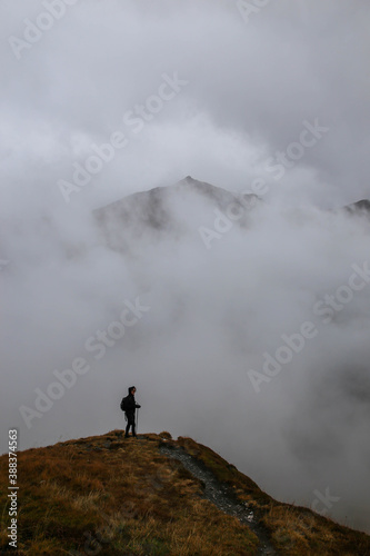 woman standing on top of mountain with view of peak in the clouds