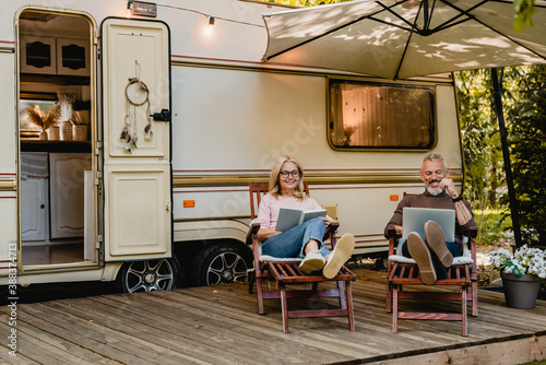 Canvastavla Senior joyful couple relaxing in the porch of thier motorhome with book and lapt