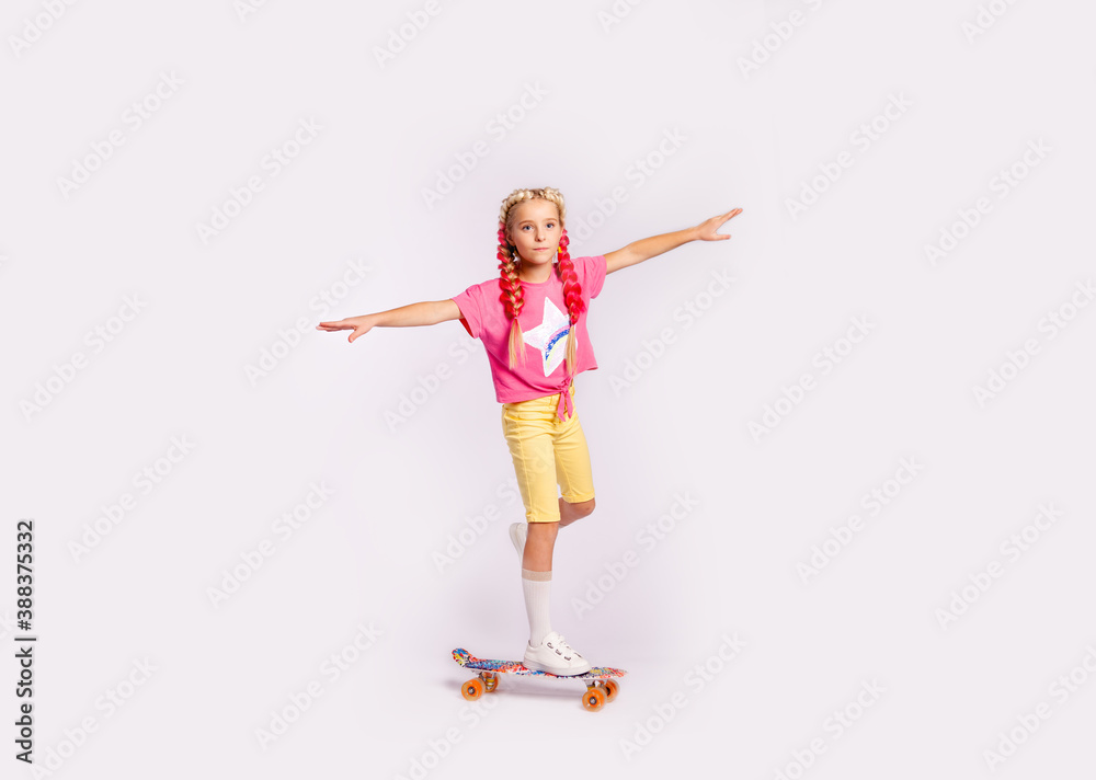 cute girl in bright colorful clothes and with colored braids performs exercises on a skateboard