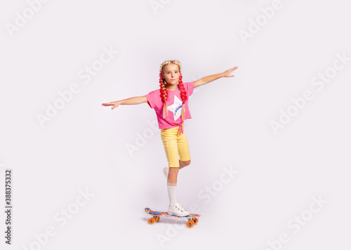 cute girl in bright colorful clothes and with colored braids performs exercises on a skateboard