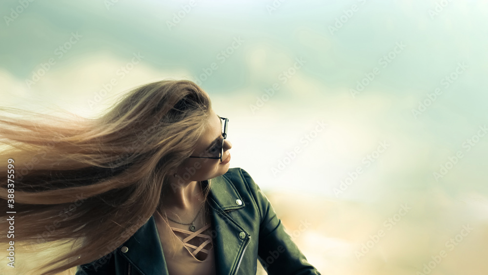 Young beautiful blonde with fluttering hair on a blue sky background Young beautiful blonde with fluttering hair on a blue sky background