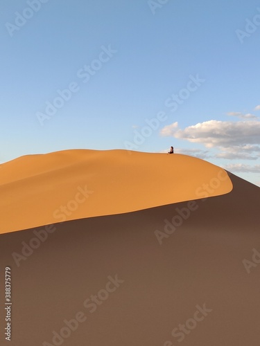 Person sitzt alleine auf einer Düne in der Wüste von Marokko