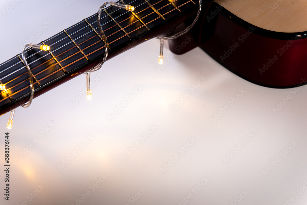 Obraz premium part of a guitar close-up wrapped in a garland on white. Concept on the theme: New Year's sale of musical instruments