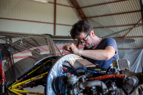 A man cheking avia oil in small aircraft. Airplane in hangar. Repaiper holding instruments near the plane engine. Small aviation.