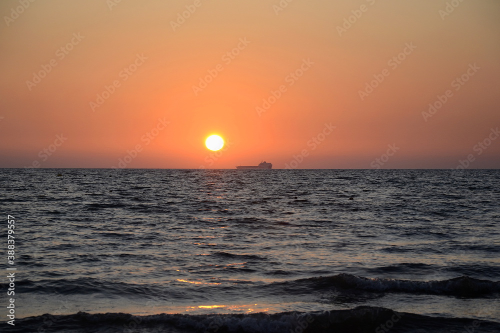 Summertime. Summer beautiful seascape. Sunset on the seashore. Pink sky at sunset. A ship on the horizon