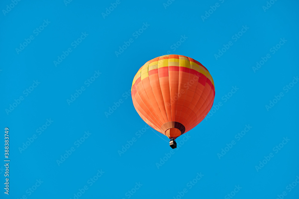 Fototapeta premium Hot-air ballon. Orange balloon in front of a shining blue sky.