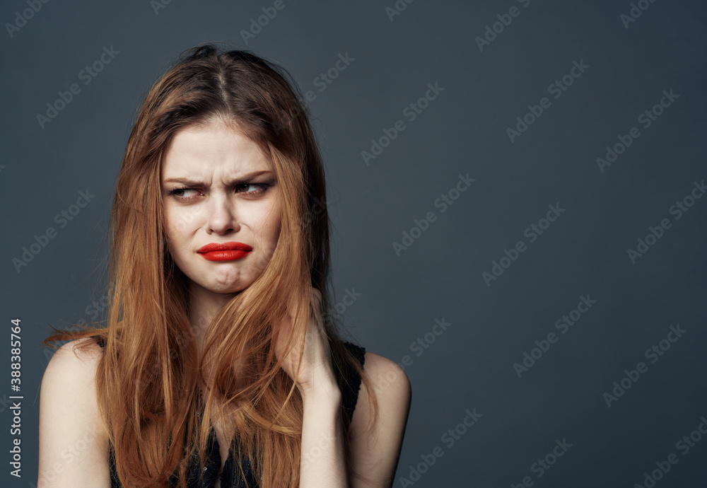 woman with red lips and in a black sundress on a gray background touches her face with her hands