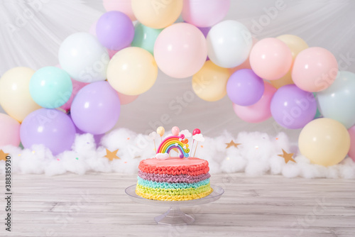 Colorful birthday cake. Rainbow cake with pastel colored balloons. Fantasy birthday. Celebration. Smash the cake photoshoot.
