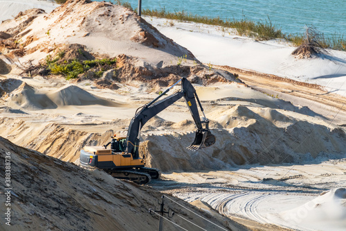 Sand extraction with machinery excavator at quartz quarry close-up. Sand dunes hills terrain digging near lake