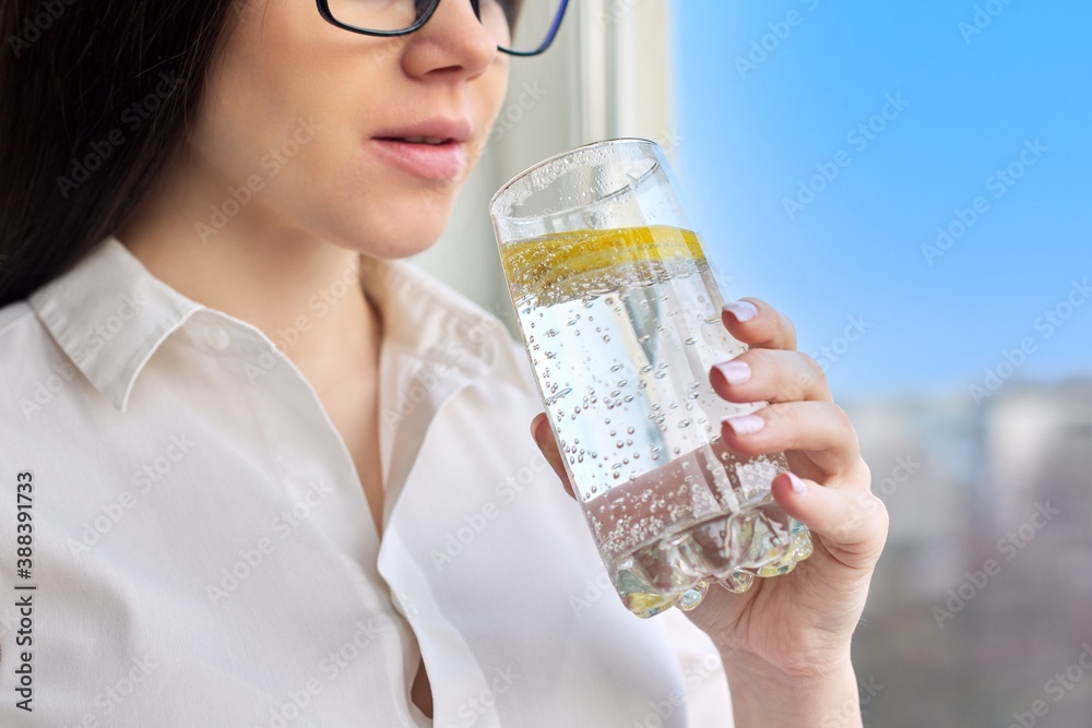 Young woman drinking mineral water with lemon in a glass at home Young woman drinking mineral water with lemon in a glass at home