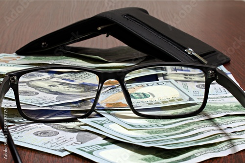 glasses on dollars on a blurred background of a wallet on the table with focus on the center