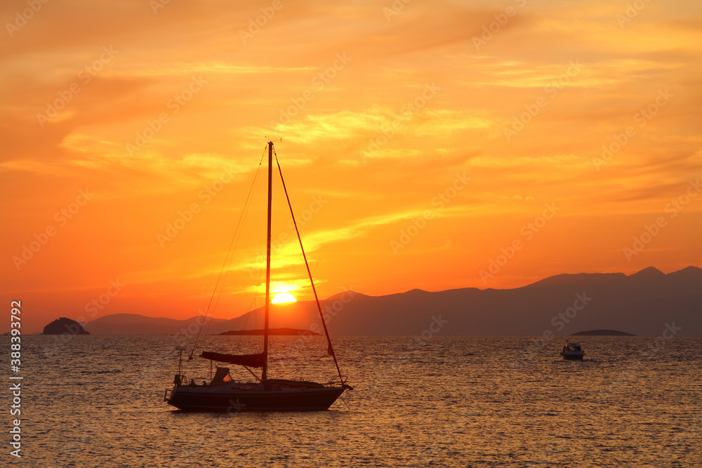 A lone sailboat at sunset. Atmospheric seascape with orange sun.