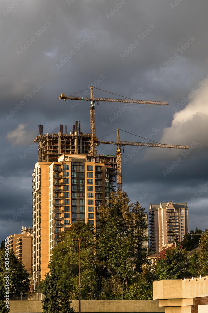 Construction of new high-rise buildings in Coquitlam City, industrial construction site, construction equipment, two construction cranes on the background of stormy cloudy sky