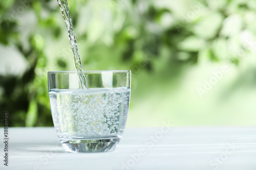 Pouring water into glass on white wooden table outdoors, space for text. Refreshing drink