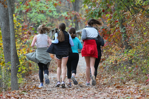 Middle school female runners running along the track among the park on a bright sunny autumn day.