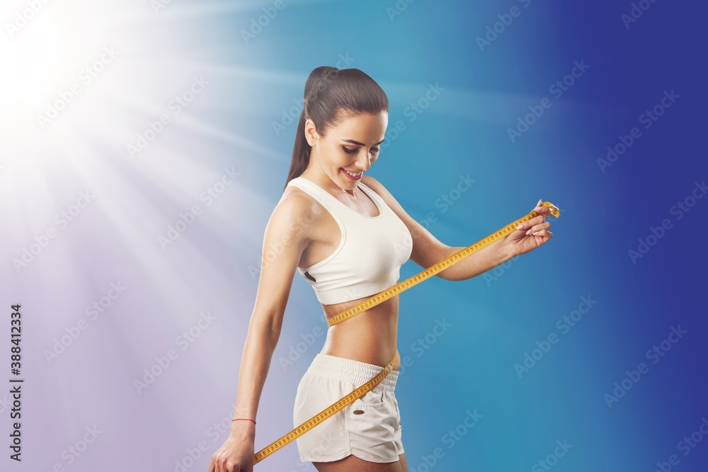 Beautiful fitness girl measuring her waistline with measure tape
