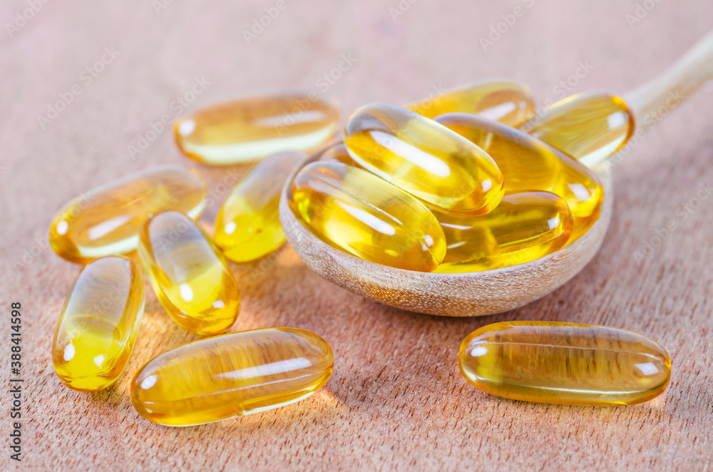 Fish oil capsules in wooden spoon on wooden.