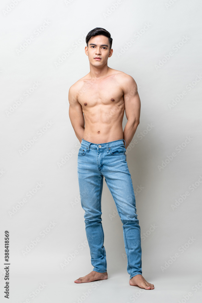 Full length portrait of muscular handsome shirtless Asian man standing and posing in light gray studio isolated background