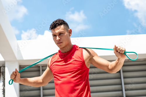 Schilderij op canvas Handsome athletic man stretching with resistance band outdoors on building rooft