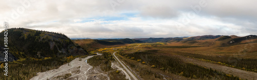 Beautiful View of Scenic Road from Above surrounded by Mountains, Trees and River Bed during Fall in Canadian Nature. Aerial Drone Shot. Taken near Dempster Highway, Yukon, Canada.