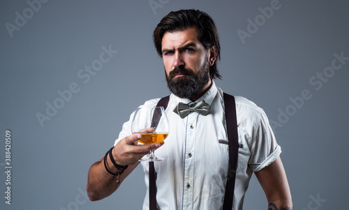 brandy or cognac. bearded man in suspenders drink scotch whiskey. brutal guy bartender wear bow tie. elegant male barman. handsome hipster drinking rum glass. party goer with alcohol