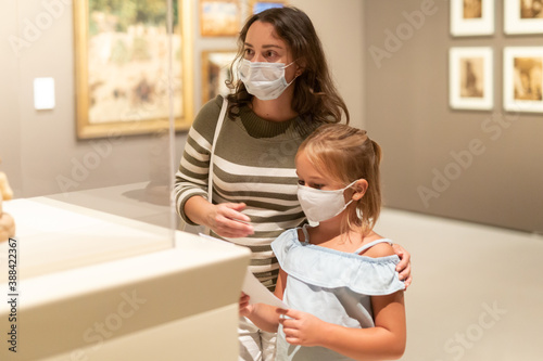 Girl with mother in masks looking with interest at art objects in museum