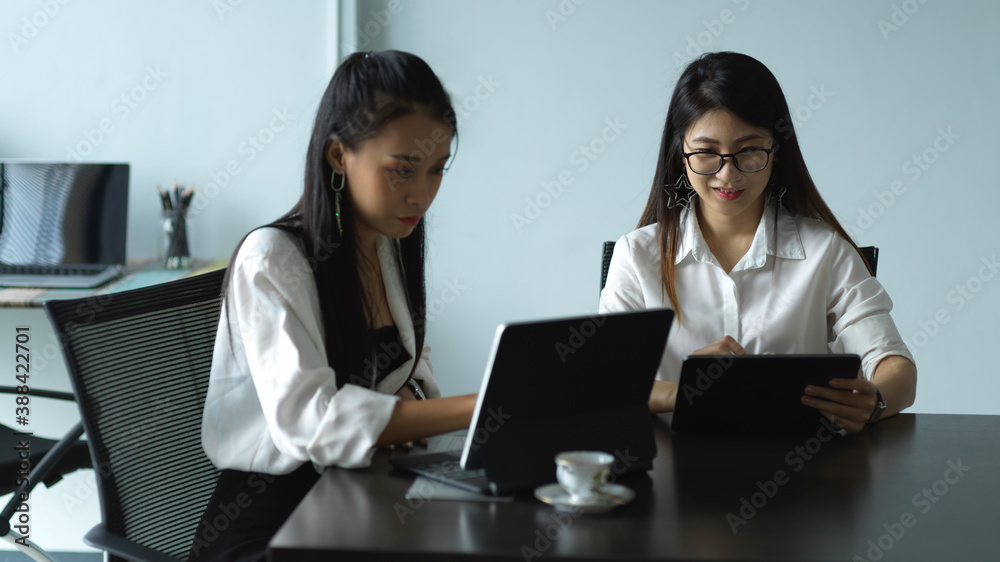 Two female workers consulting on their work with tablet in meeting room Two female workers consulting on their work with tablet in meeting room