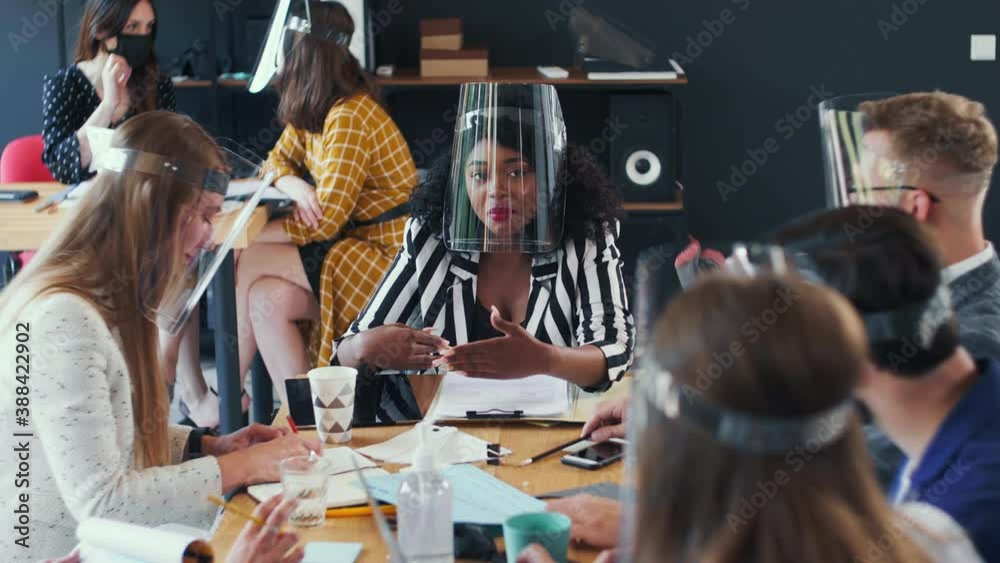Happy successful gen-z African female coach leads office team meeting, everyone wearing coronavirus safety face shields. Happy successful gen-z African female coach leads office team meeting, everyone wearing coronavirus safety face shields.