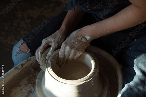 Hands of woman working with pottery wheel and making ceramic chamotte vase on it. dark and light