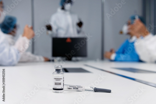 Coronavirus covid 19 vaccine sample in a clean laboratory meeting room with a background of coronavirus covid 19 disease experts discussion with protective suit, mask and gloves