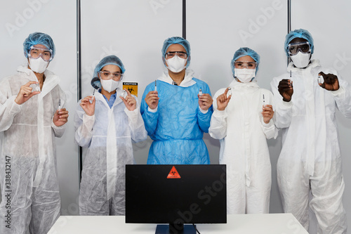 Diversity coronavirus covid 19 disease experts in a clean laboratory meeting room show samples of coronavirus covid 19 vaccine labelled coronavirus covid 19 with protective suit, mask and gloves