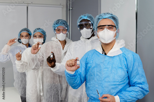 Diversity coronavirus covid 19 disease experts in a clean laboratory meeting room show samples of coronavirus covid 19 vaccine labelled coronavirus covid 19 with protective suit, mask and gloves