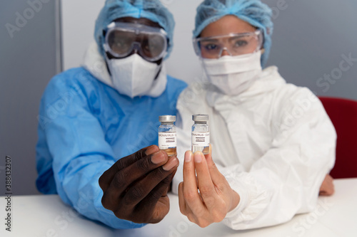 Coronavirus covid 19 disease experts hold samples of coronavirus covid 19 vaccine sample labelled coronavirus covid 19 with confidence and protective suit, mask and gloves