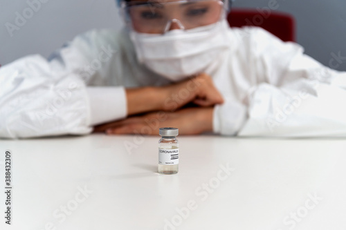 Coronavirus covid 19 disease expert look at a sample of coronavirus covid 19 vaccine sample labelled coronavirus covid 19 with confidence and protective suit, mask and gloves