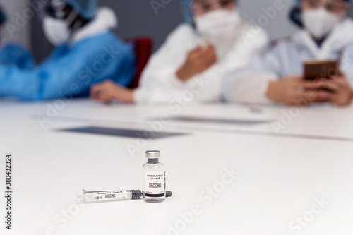 Coronavirus covid 19 vaccine sample in a clean laboratory meeting room with a background of coronavirus covid 19 disease experts discussion with protective suit, mask and gloves