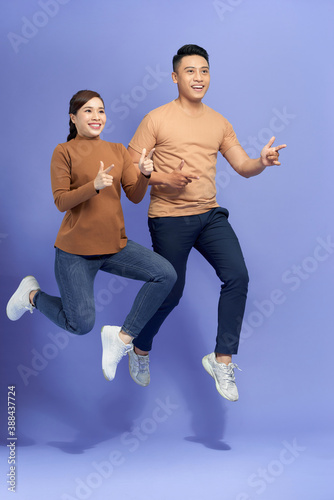 Photo of happy young loving couple jumping isolated over purple background showing thumbs up.