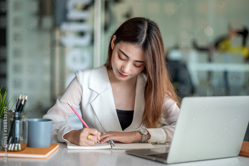 Beautiful asian businesswoman or financial manager working in modern office on laptop. Businesswoman working on laptop and taking note while sitting at the table in office. Beautiful asian businesswoman or financial manager working in modern office on laptop. Businesswoman working on laptop and taking note while sitting at the table in office.